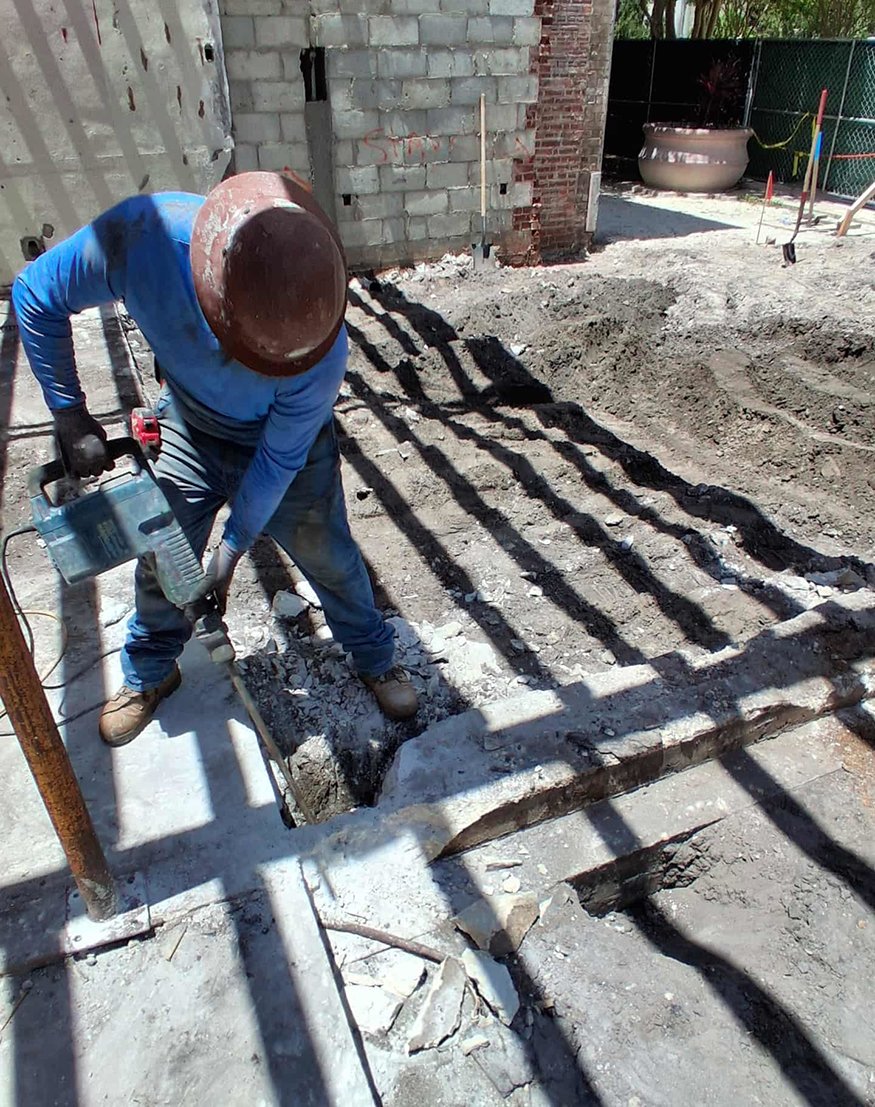 Worker removes concrete footing sections with demolition equipment.