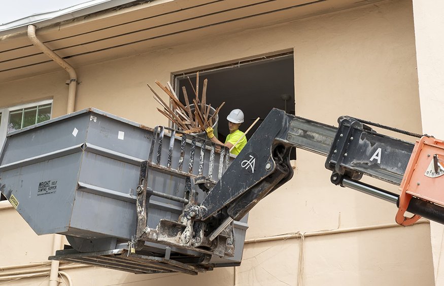 Worker loads wood framing into lift bucket from second floor window.