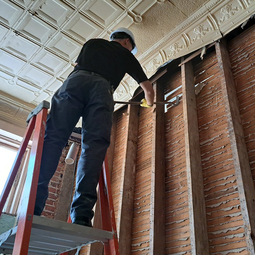 Crew removes interior wood and stucco wall to expose original framing.