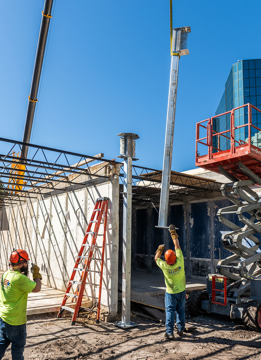 Workers guide a suspended steel column into position.