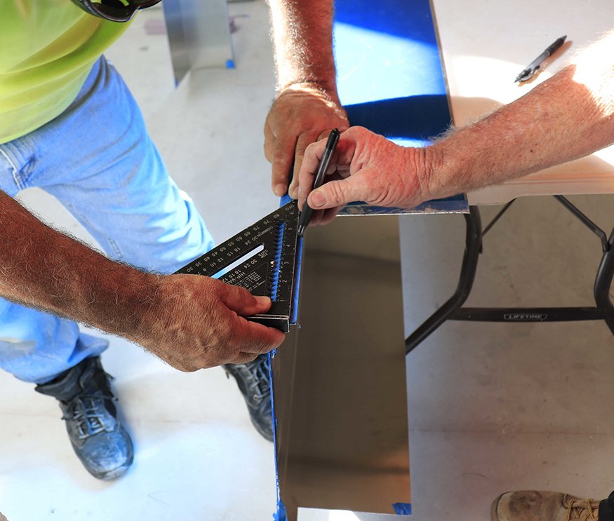Workers measuring brass panel for door frame.