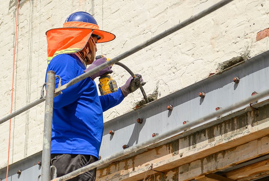 Worker using concrete vibrator tool on poured concrete.