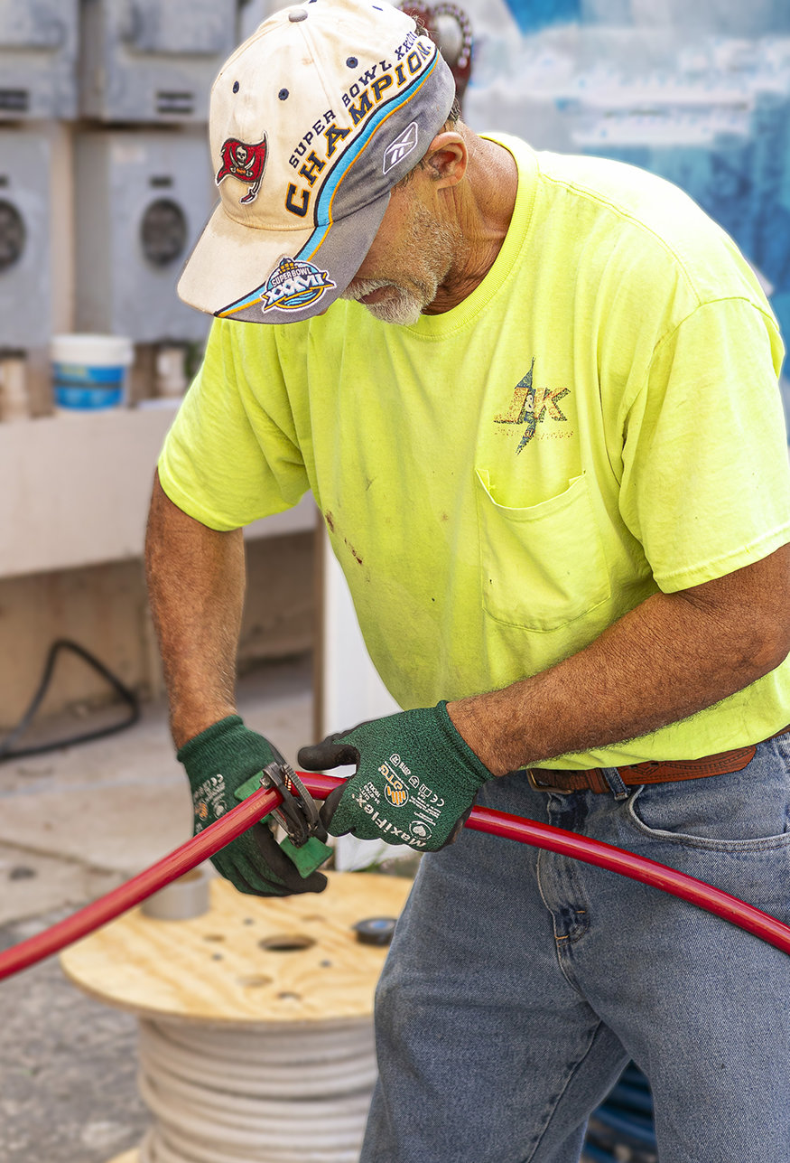 Worker cutting red electrical cable outdoors