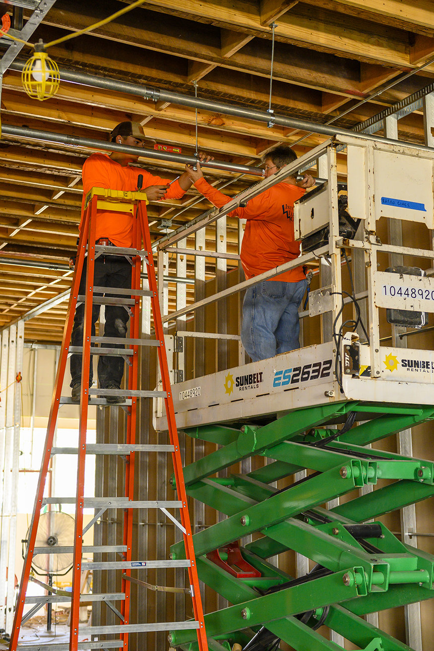 Electricians on lift installing conduit.