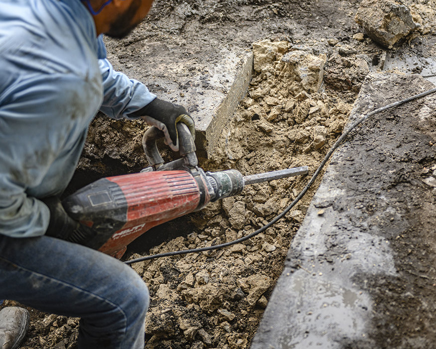 Worker uses demolition hammer to break existing wall foundation.