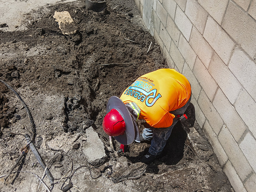 Worker hand-digs trench for underground plumbing.