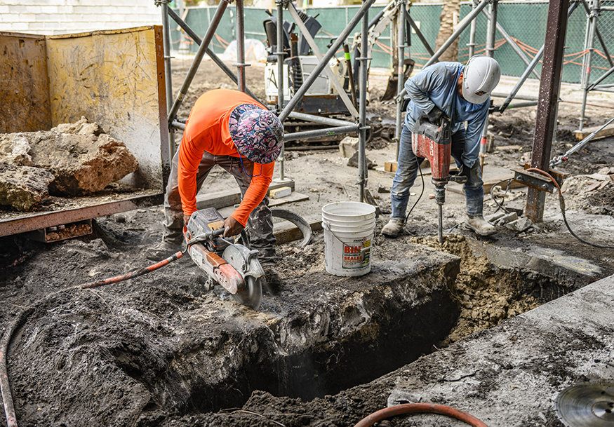 Workers remove former wall foundation with demolition tools.