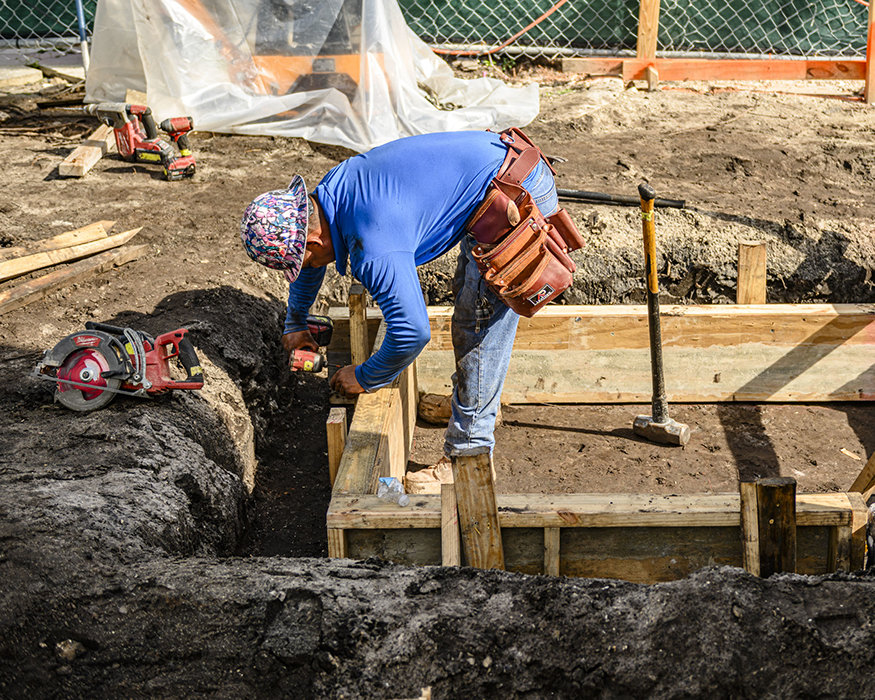 Worker fastens wood form for new footing.