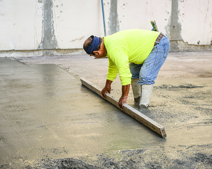 Worker levels freshly poured concrete with straightedge.