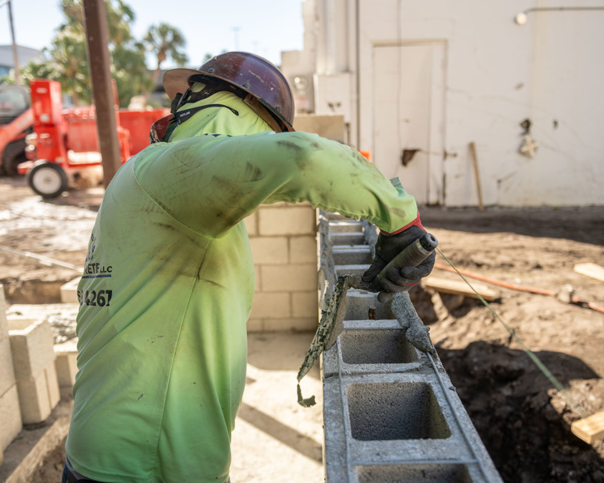 Mason applies mortar along top of concrete wall.