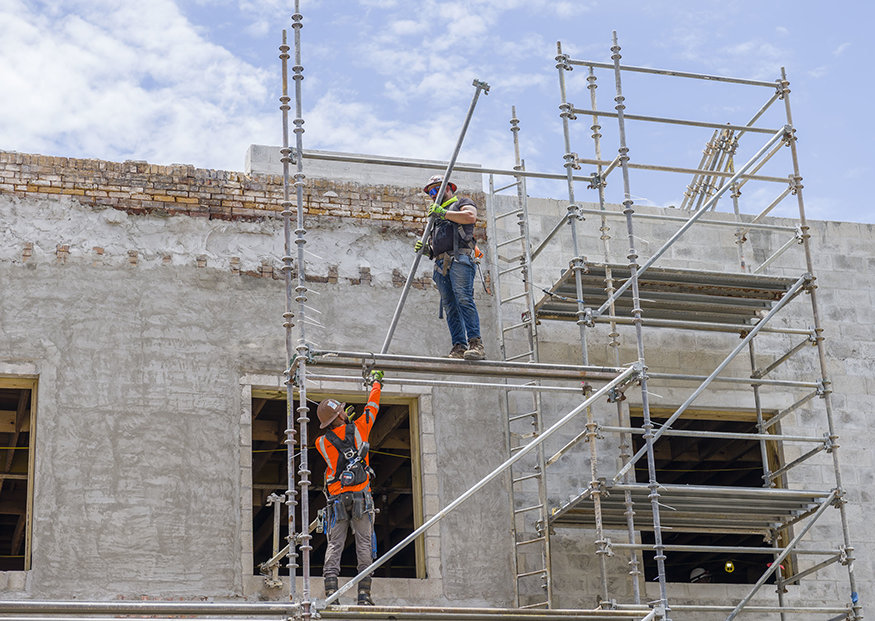 Construction workers lowering scaffold pole on the side of the Peoples Bank.