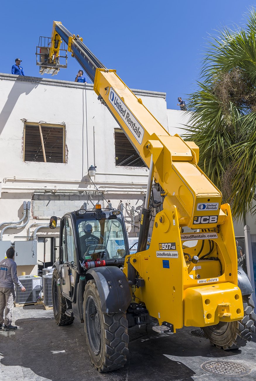 Telehandler hoisting an A/C unit to the rooftop.