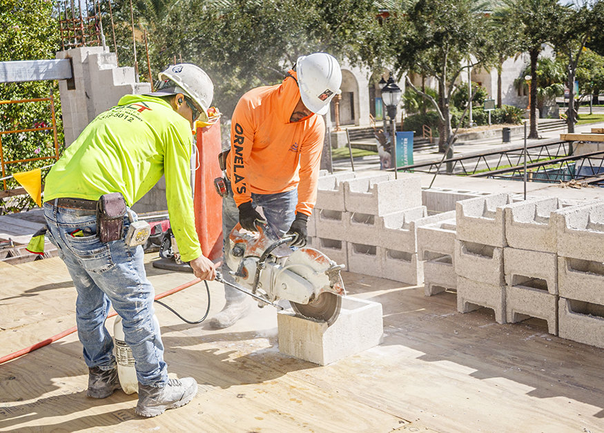 Worker cuts concrete masonry unit for parapet.