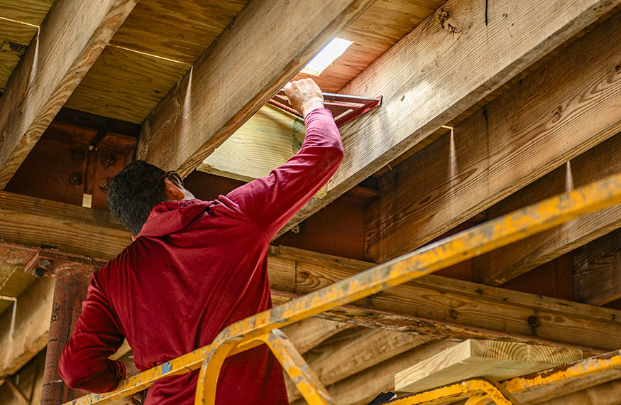 Carpenter measures wood blocking between roof joists.