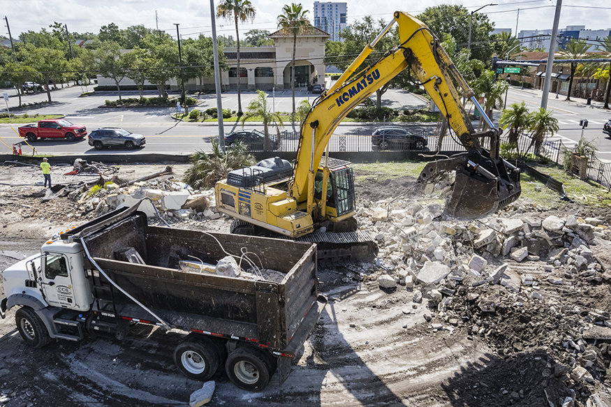 Excavator loading broken concrete foundation material into a dump truck during demolition and site-clearing operations.