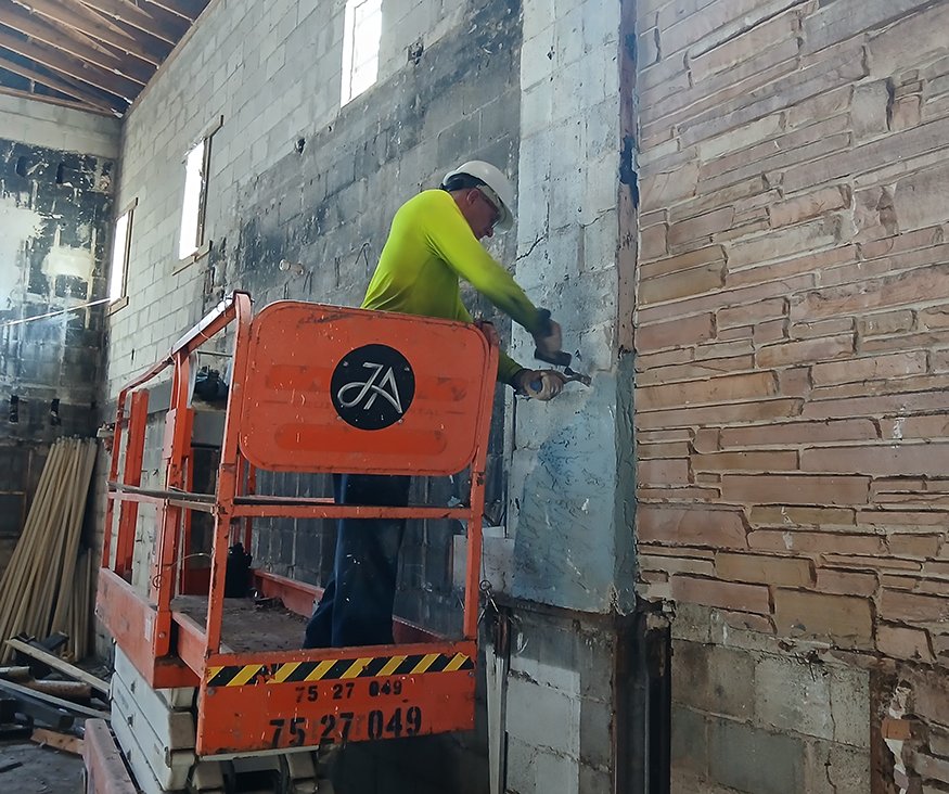 Worker chipping brick interior wall with chisel and hammer.