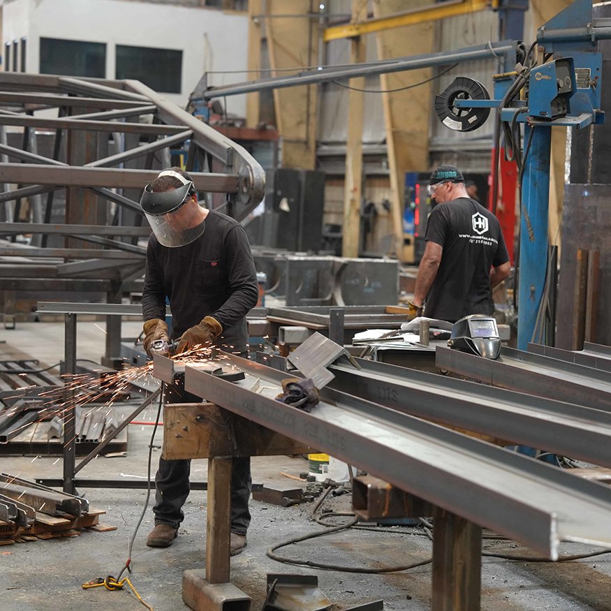 Fabricator grinds structural steel components in shop.