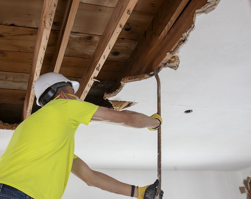 A pry bar is used to dismantle ceiling drywall.