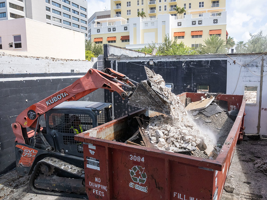 Loader dumps roofing debris into a construction dumpster.