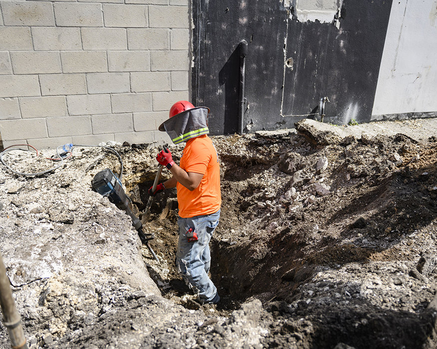 Worker prepares plumbing trench with hand tools.