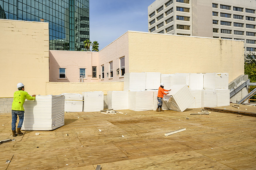 Workers move insulation pallets across new roof deck.