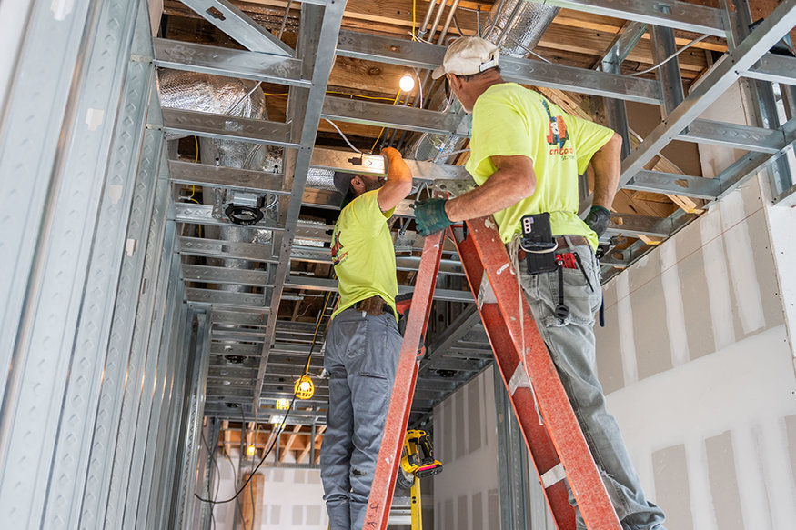 Electricians working inside ceiling framing installing wires.