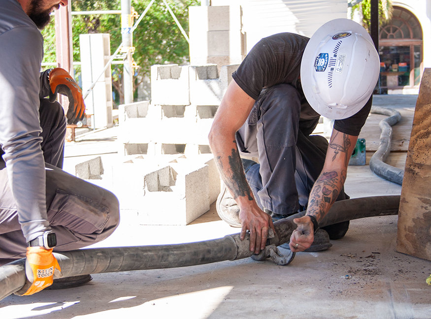 Workers assemble concrete-pumping hose for new masonry wall.