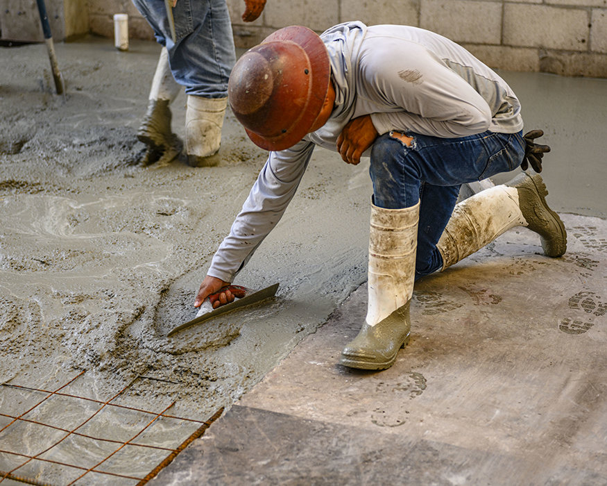 Worker smooths fresh concrete with hand trowel.