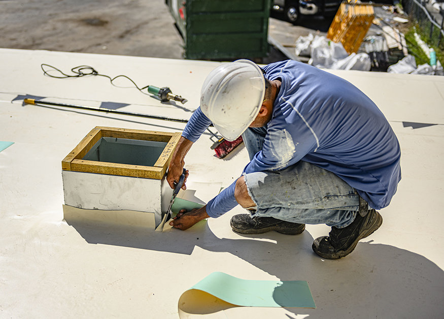 Worker fits roofing membrane around rooftop opening.
