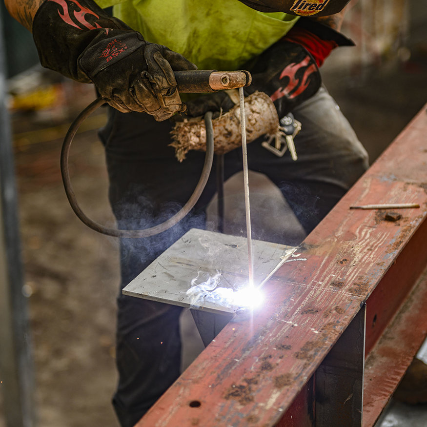 Welder joins steel bracket to structural beam.