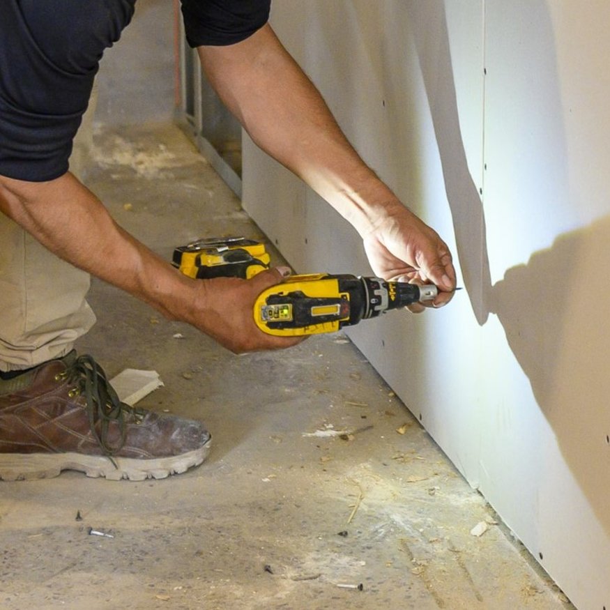 Worker installing drywall on framed wall.