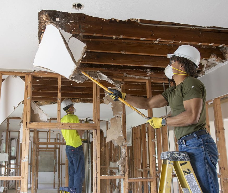 Workers removing ceiling to access roof structure.