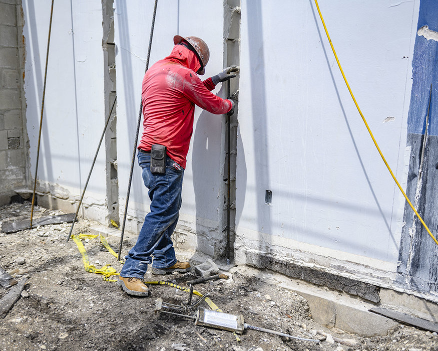 Worker positions rebar inside an existing concrete masonry wall.