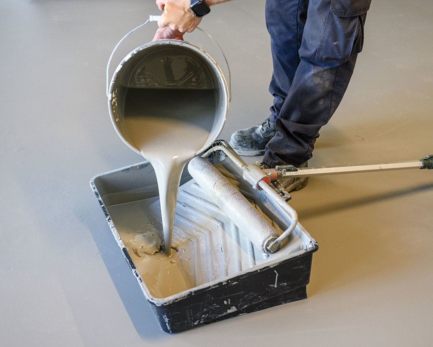 Worker pouring concrete stain into tray.