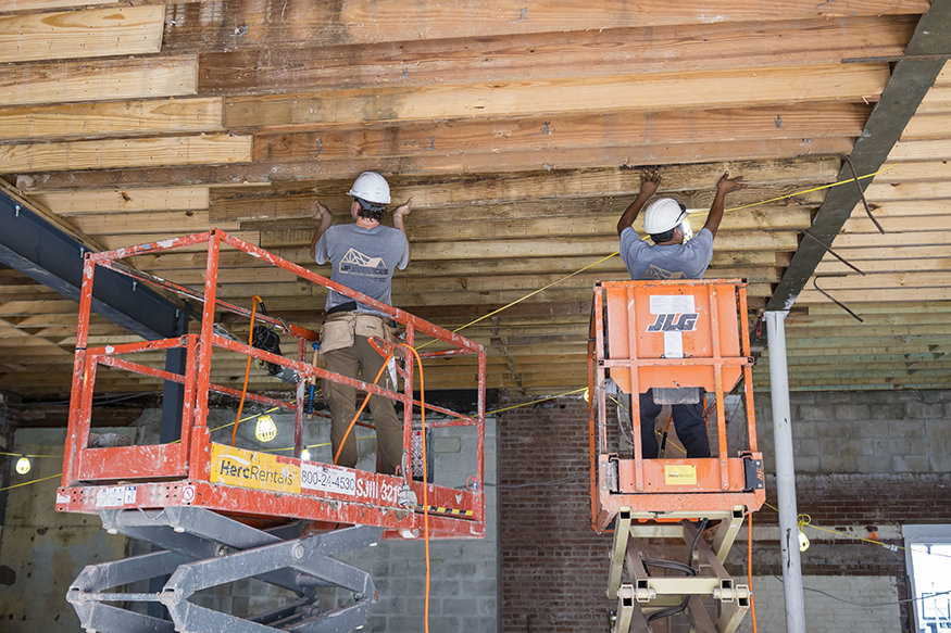 Two men working from lifts to adjust wood decking on underside of second floor.