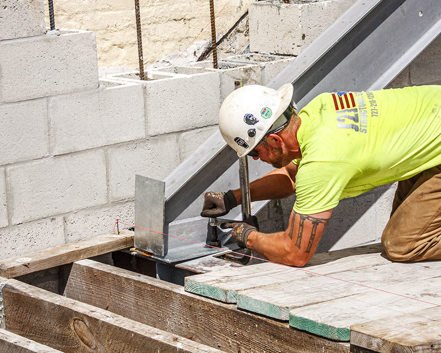 Worker secures angled steel beam at entry frame.