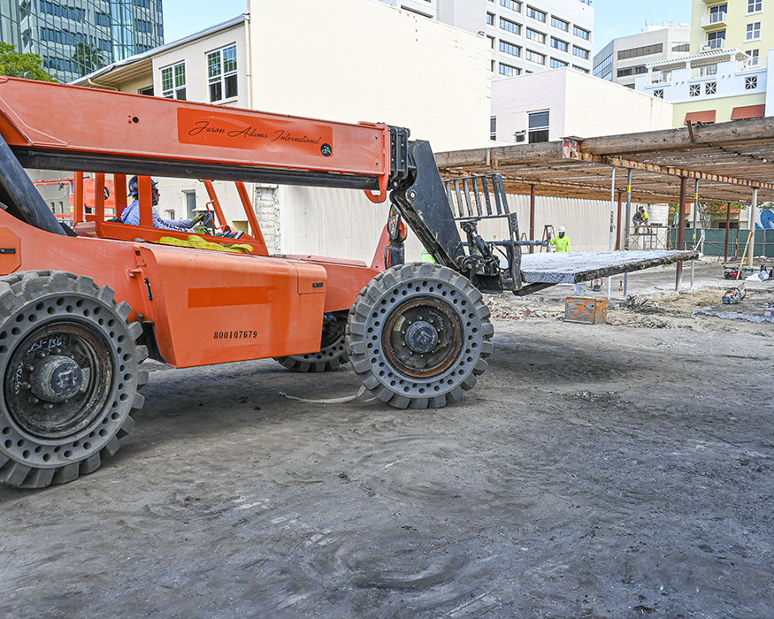 Telehandler removes concrete slab sections during plumbing trenching.