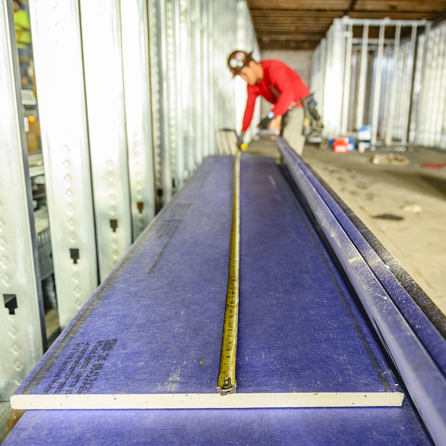 Worker measures a shaft-wall liner panel for interior framing.