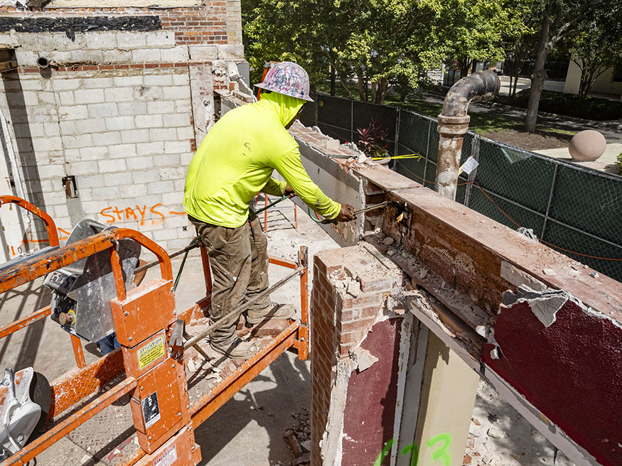 Crew member cuts façade wall from lift.