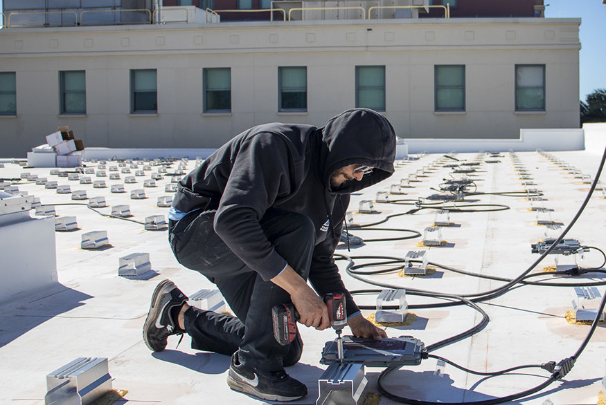 Rooftop work continues as equipment is secured ahead of panel installation.