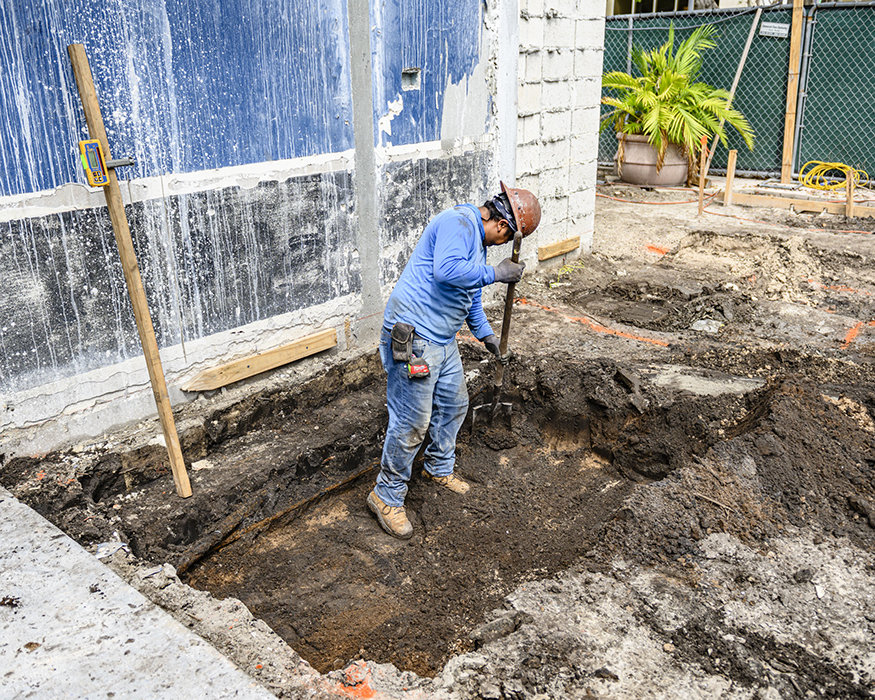 Worker removes soil within new footing excavation.