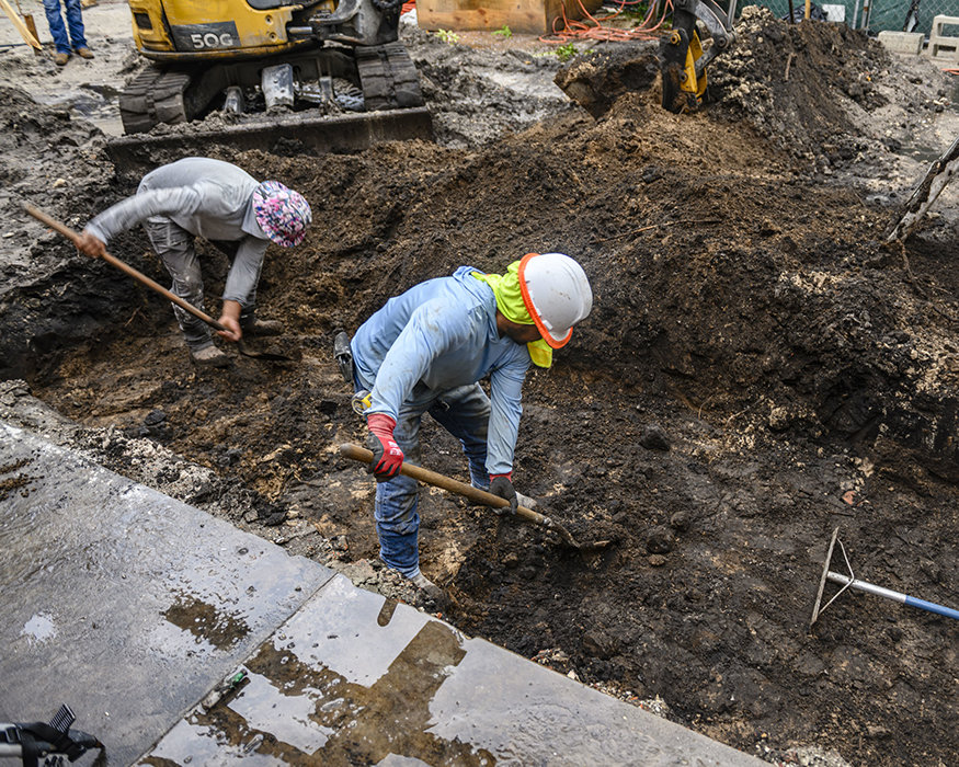 Workers use hand tools in foundation excavation area.