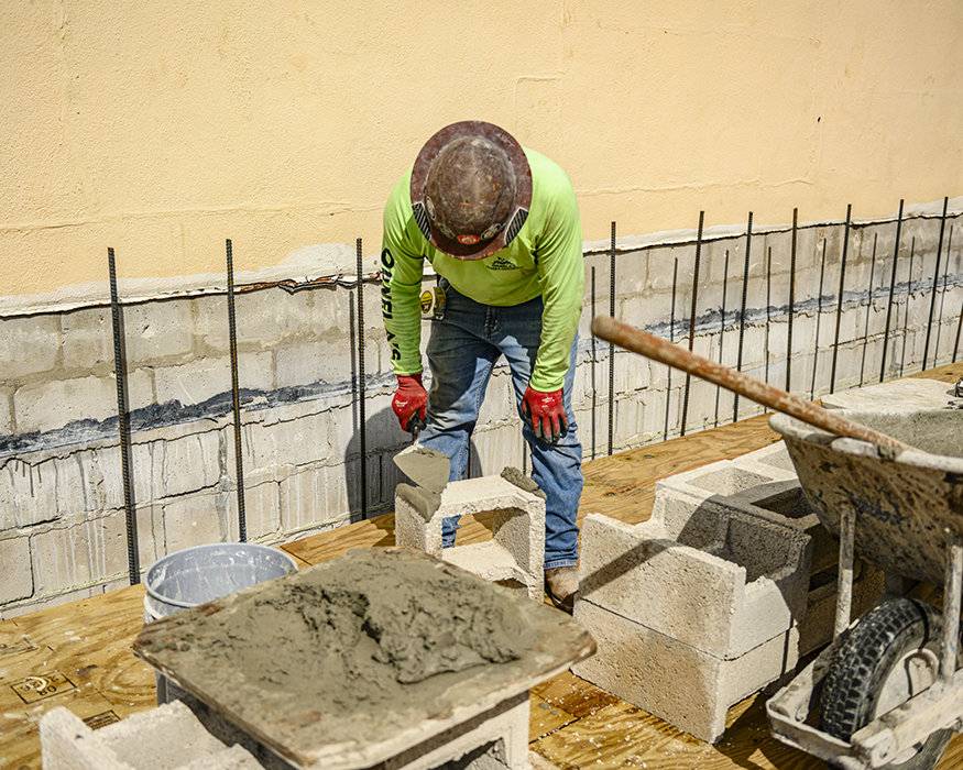 Worker applies mortar to concrete block before placement.