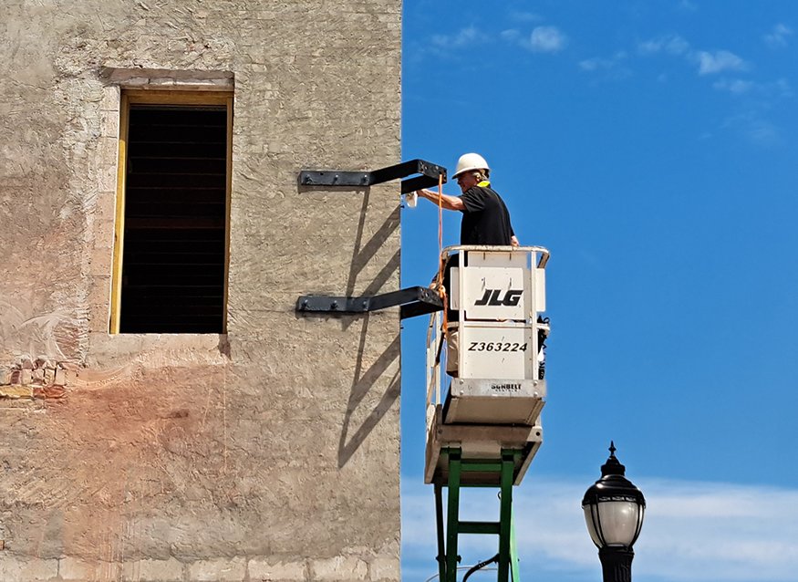 Worker fastening steel clock bracket to building façade.
