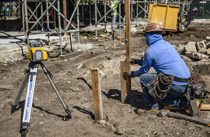 Worker positions foundation stake beside surveying instrument.