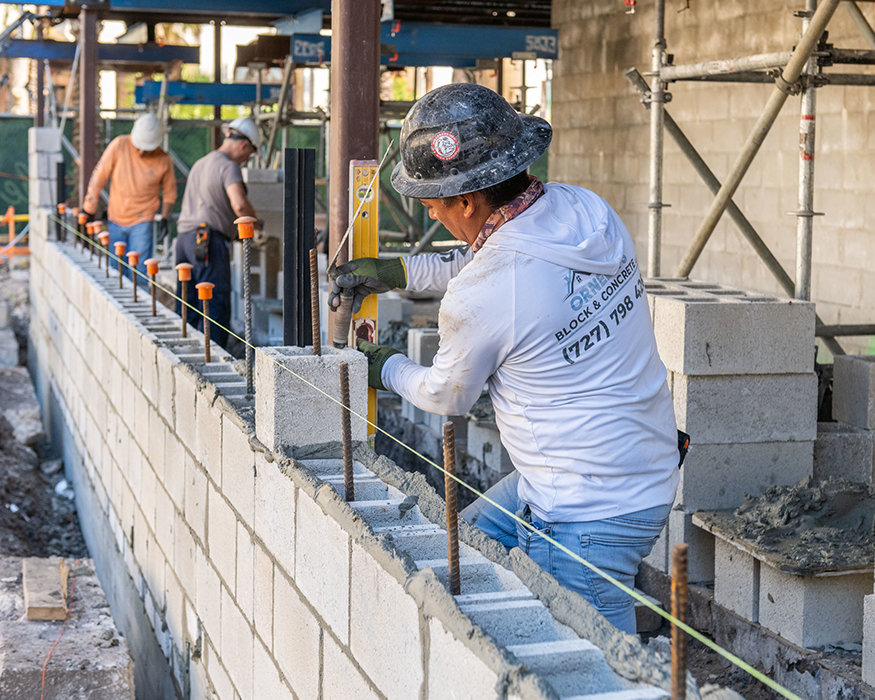 Worker positions concrete masonry unit and checks alignment with level.