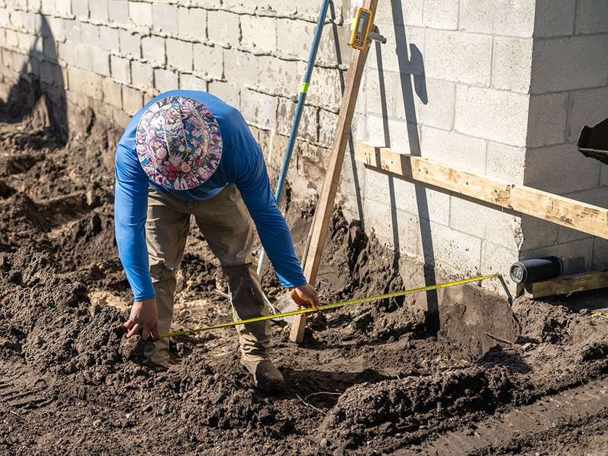 Worker measures area for new wall footing.