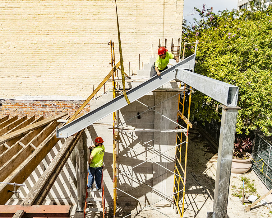 Workers align suspended steel beam with new frame.