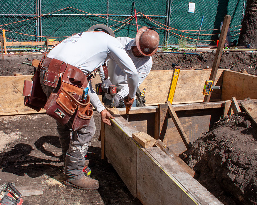 Workers secure wood formwork for wall footing.