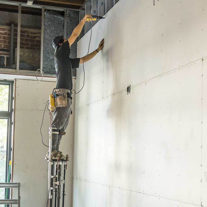 Worker on stilts installing drywall.